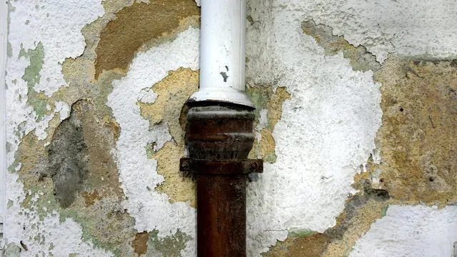 Water-damaged peeling drywall around a pipe