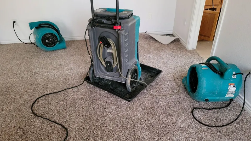 Air movers and a dehumidifier running on carpet to dry a water-damaged room